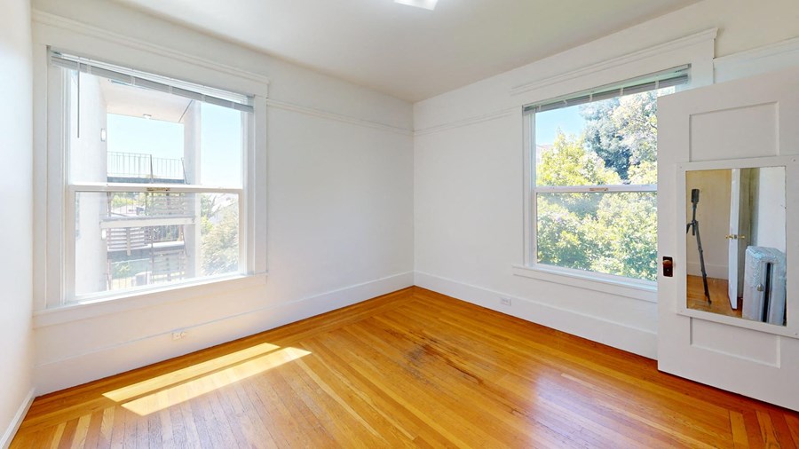 an empty room with wooden floors and two windows